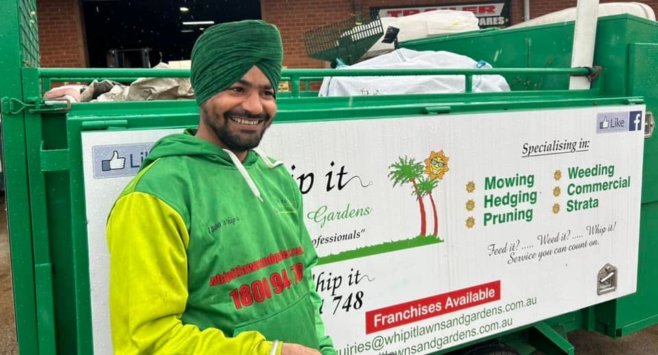 A man in a turban is standing next to a green dumpster.