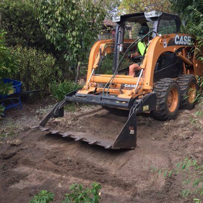 A man is driving a case skid steer loader on a dirt road.