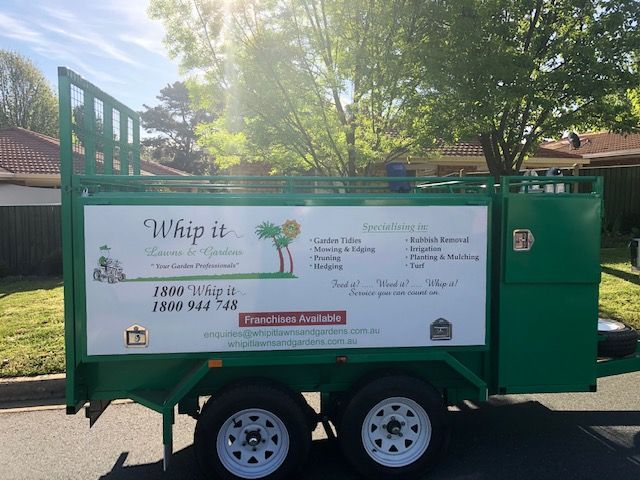A green trailer with a white sign that says whip it is parked on the side of the road.
