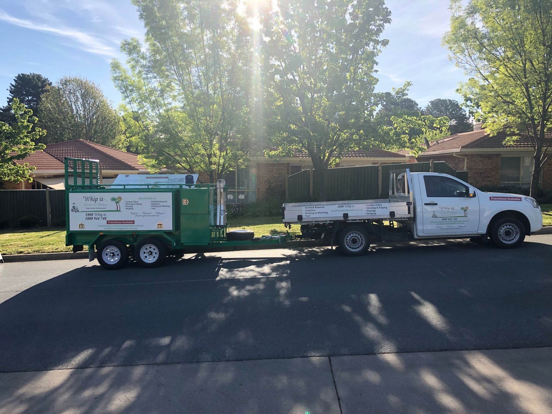 A white truck with a green trailer attached to it is parked on the side of the road.