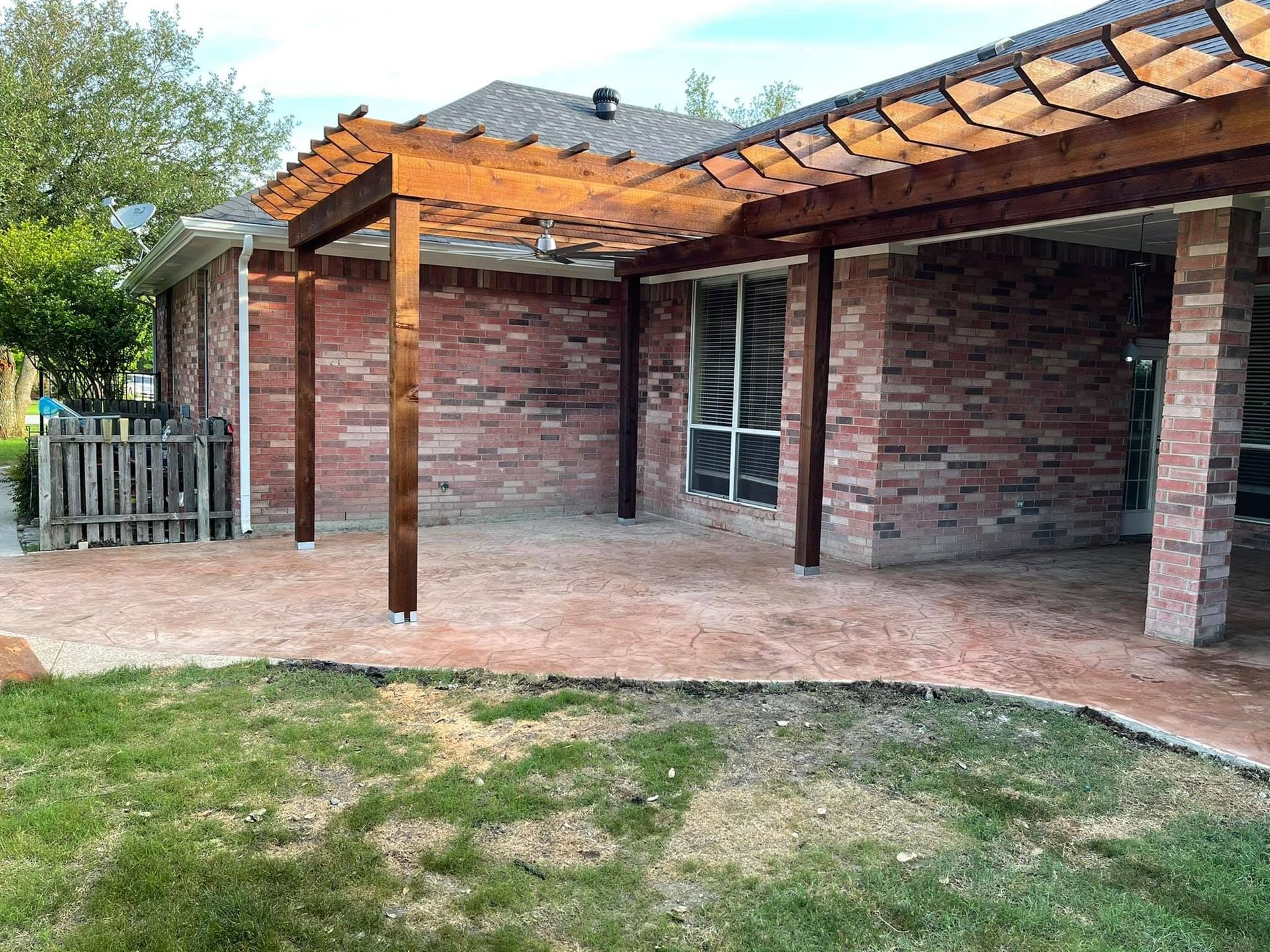 Pergola over a brick patio in a backyard with a grassy lawn.