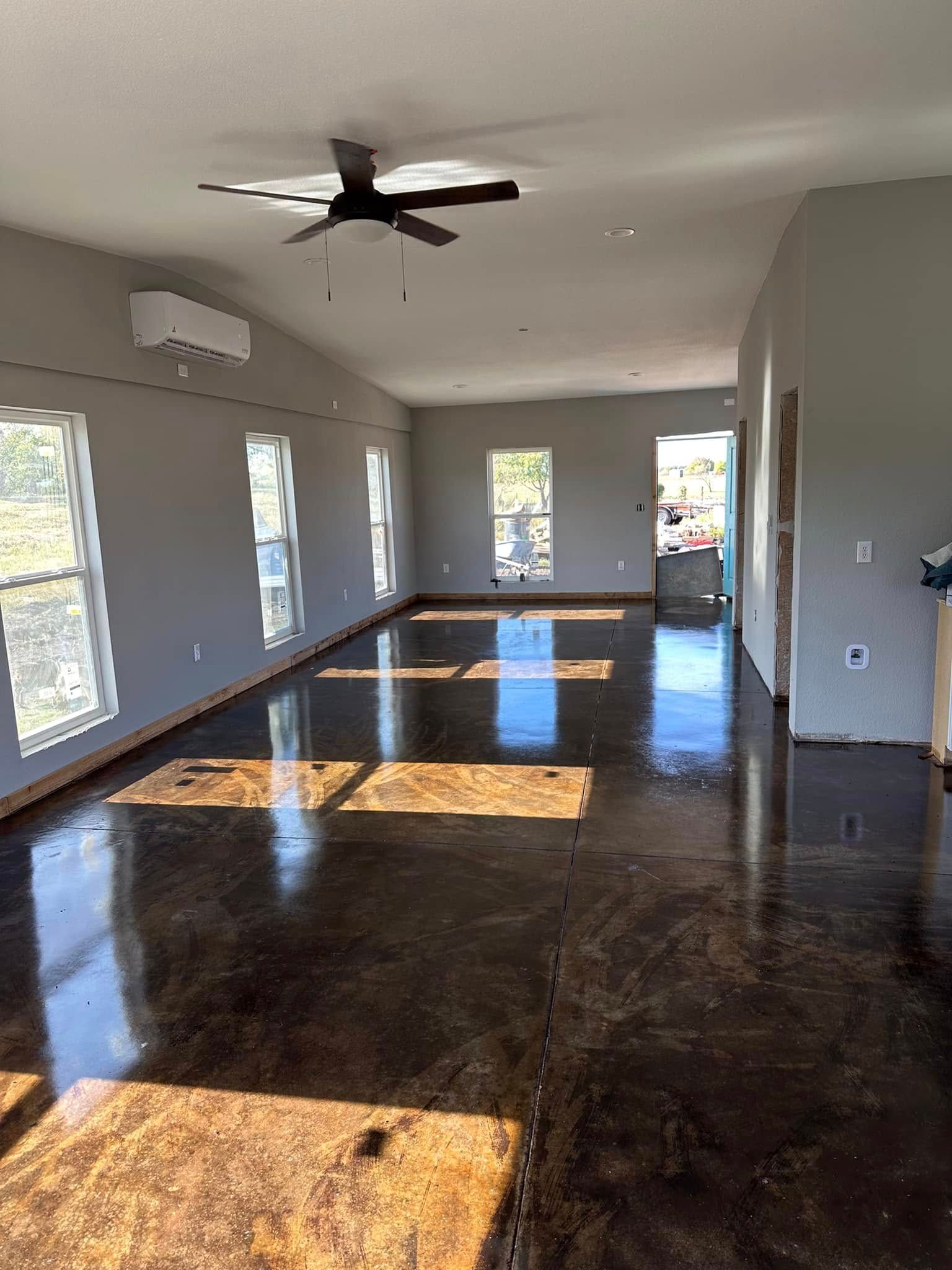 Spacious, light-filled room with shiny dark floors, gray walls, and several windows. A ceiling fan hangs overhead.