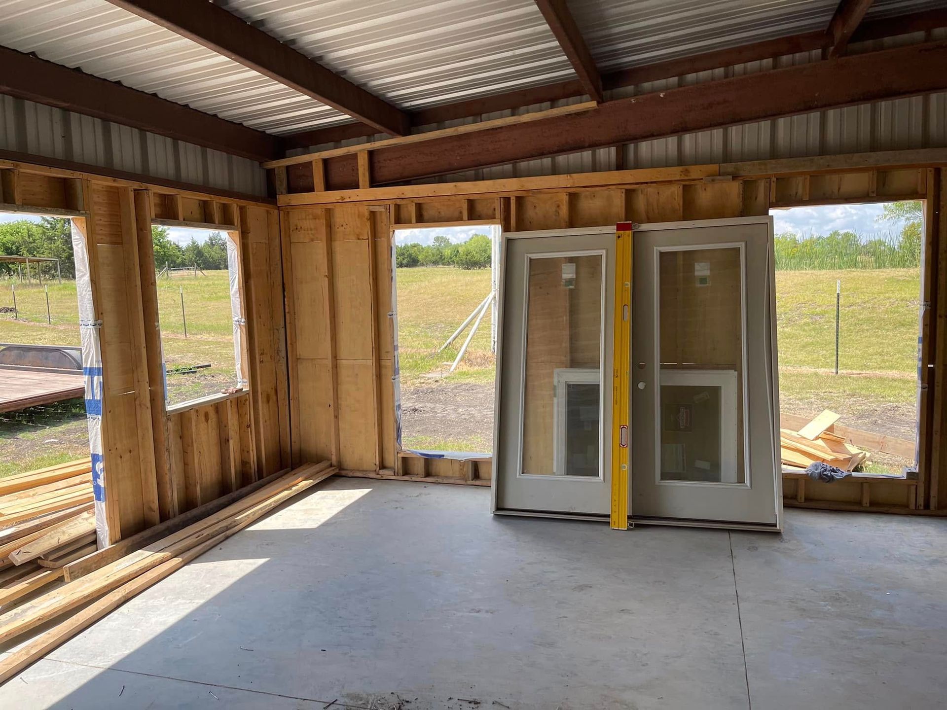 Interior of a building under construction, wood framing and concrete floor, with doors and windows.
