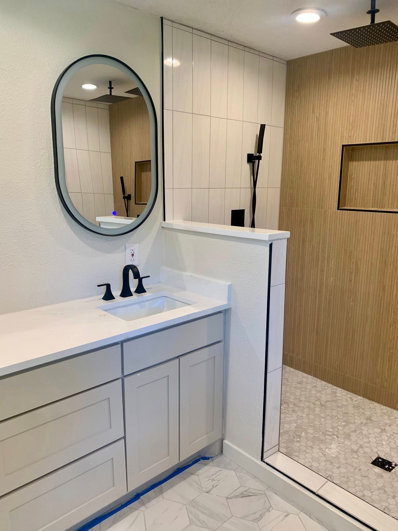 Modern bathroom with white vanity, oval mirror, walk-in shower with brown wood-look tile.
