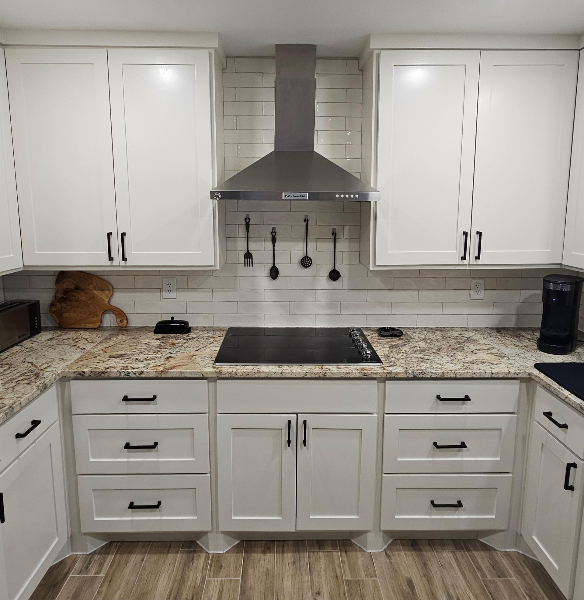 White kitchen cabinets with black hardware and a stainless steel range hood over a black stovetop.