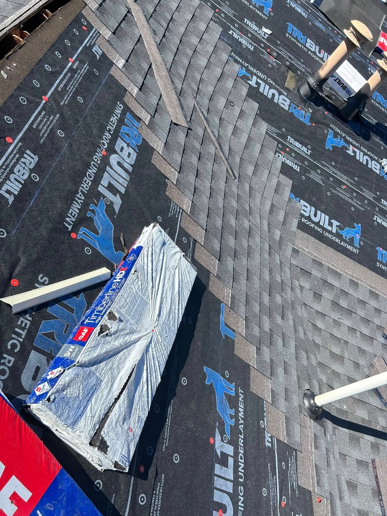 Roofing work in progress, dark shingles being installed, close-up view of the corner.