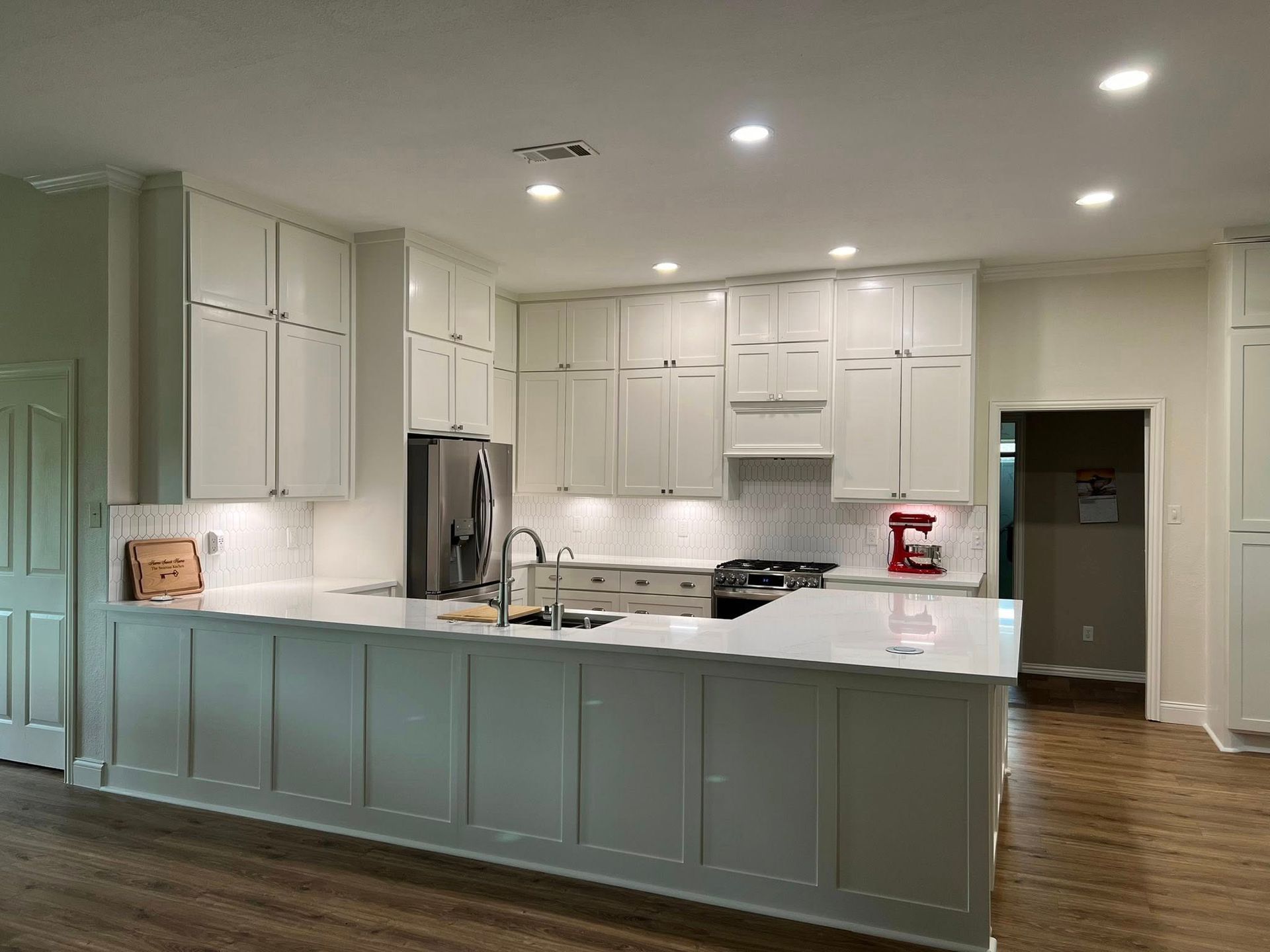 White kitchen with cabinets, island, stainless steel appliances, and hardwood floor.