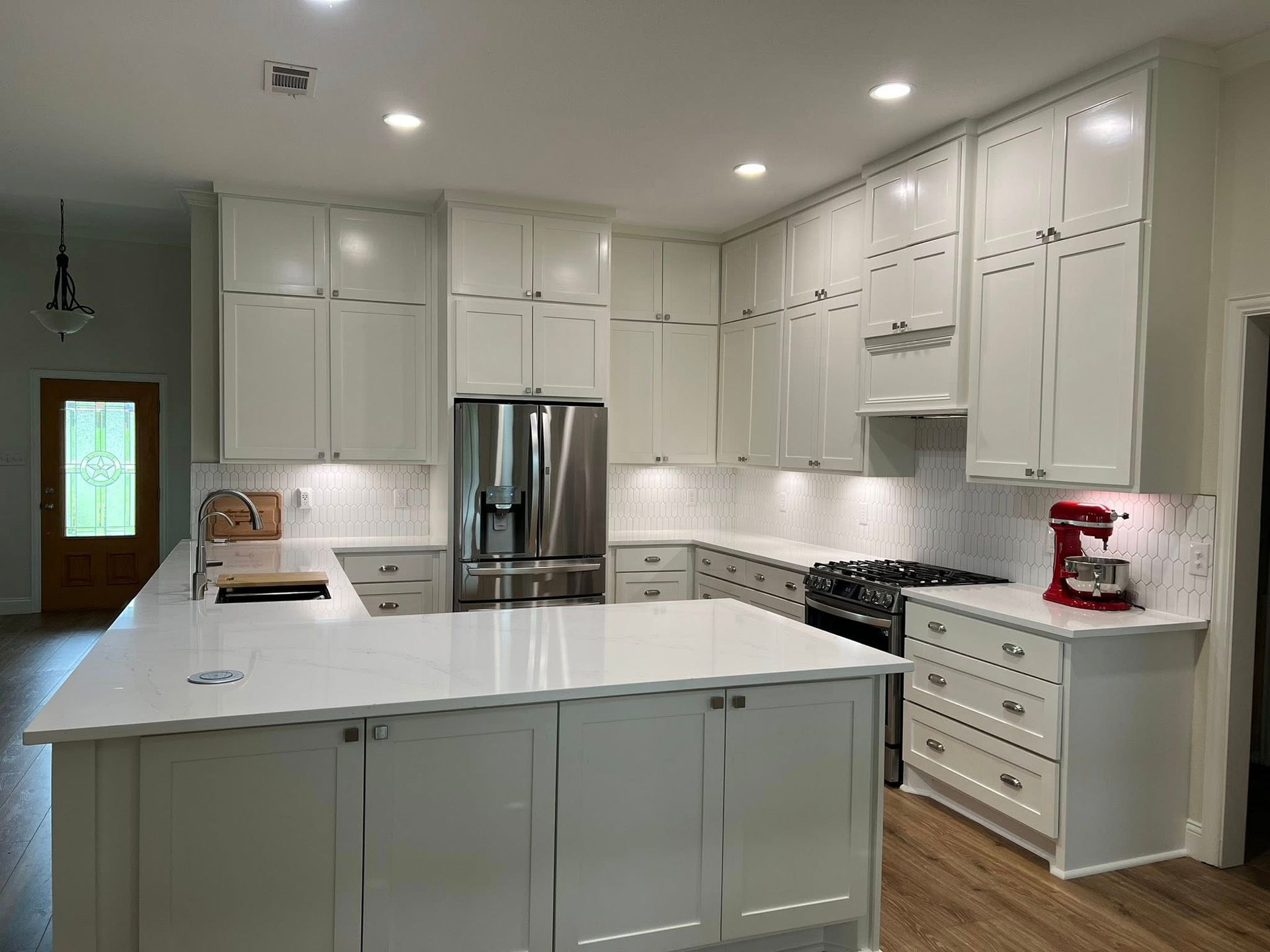 White kitchen with island, cabinets, stainless steel refrigerator, and stovetop.