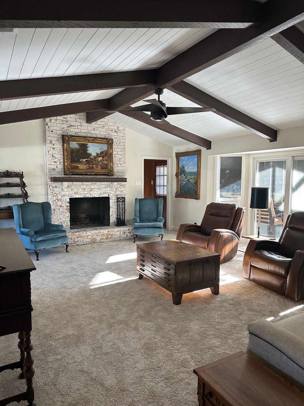 Spacious living room with vaulted ceilings, exposed beams, a stone fireplace, blue armchairs, and leather recliners.