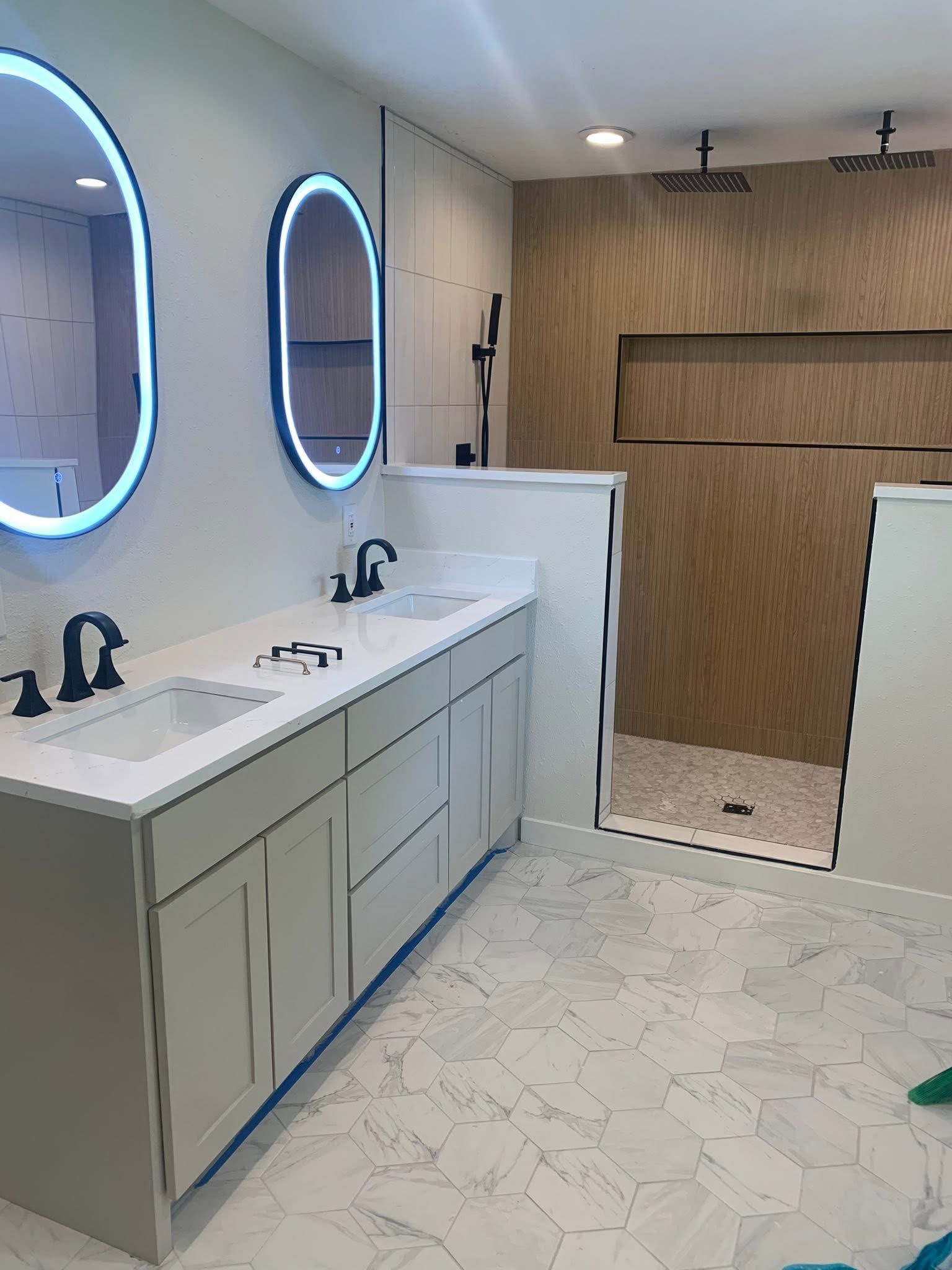 A modern bathroom featuring a white vanity with a black faucet, a curved mirror, and a walk-in shower with wood-look tile.