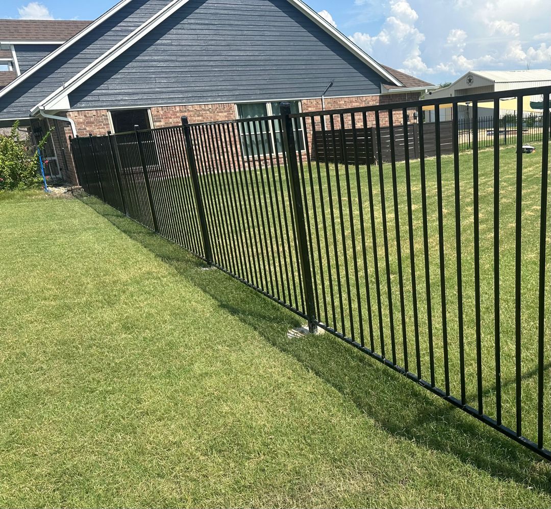 A dark metal fence in the foreground sits before a taller, horizontal wood plank privacy fence bordering an empty lot.