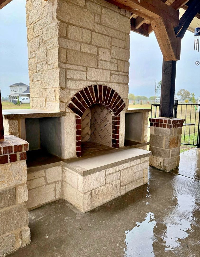 A covered outdoor patio featuring a stone fireplace with a mounted television, a granite bar, and comfortable seating.