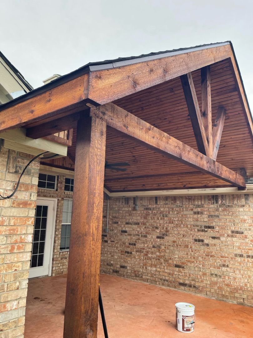 A ceiling fan hanging from a wooden, vaulted porch ceiling, positioned next to a brick exterior wall.