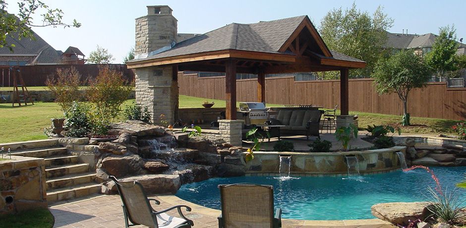 Backyard with pool, waterfall, gazebo with seating, and stone fireplace. Sunny day.