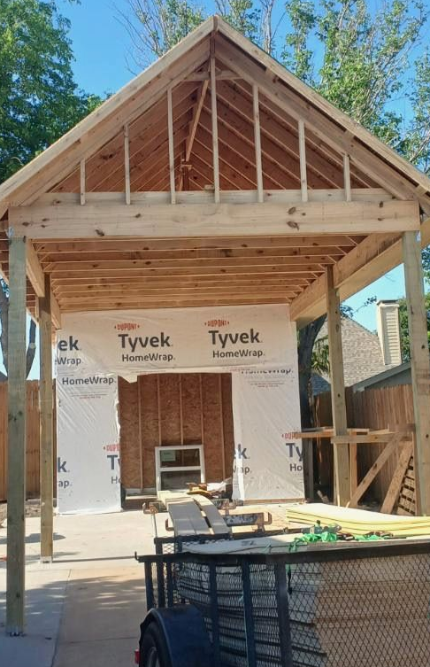 Unfinished interior room with wooden wall studs, exposed ceiling beams, a concrete floor, and two large window openings.
