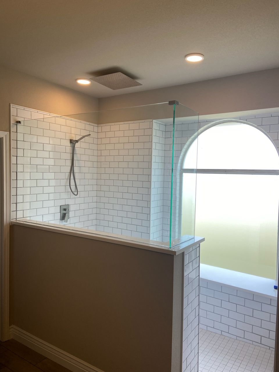 Bathroom with white brick-style tile, glass shower door, and arched window with a frosted privacy covering.