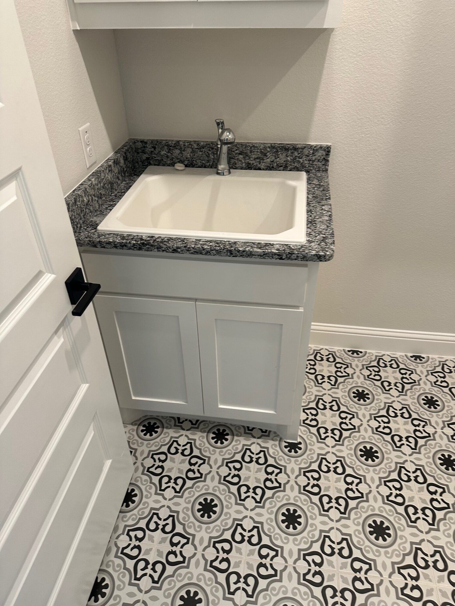 White cabinet with a utility sink and granite countertop, next to a patterned tile floor.