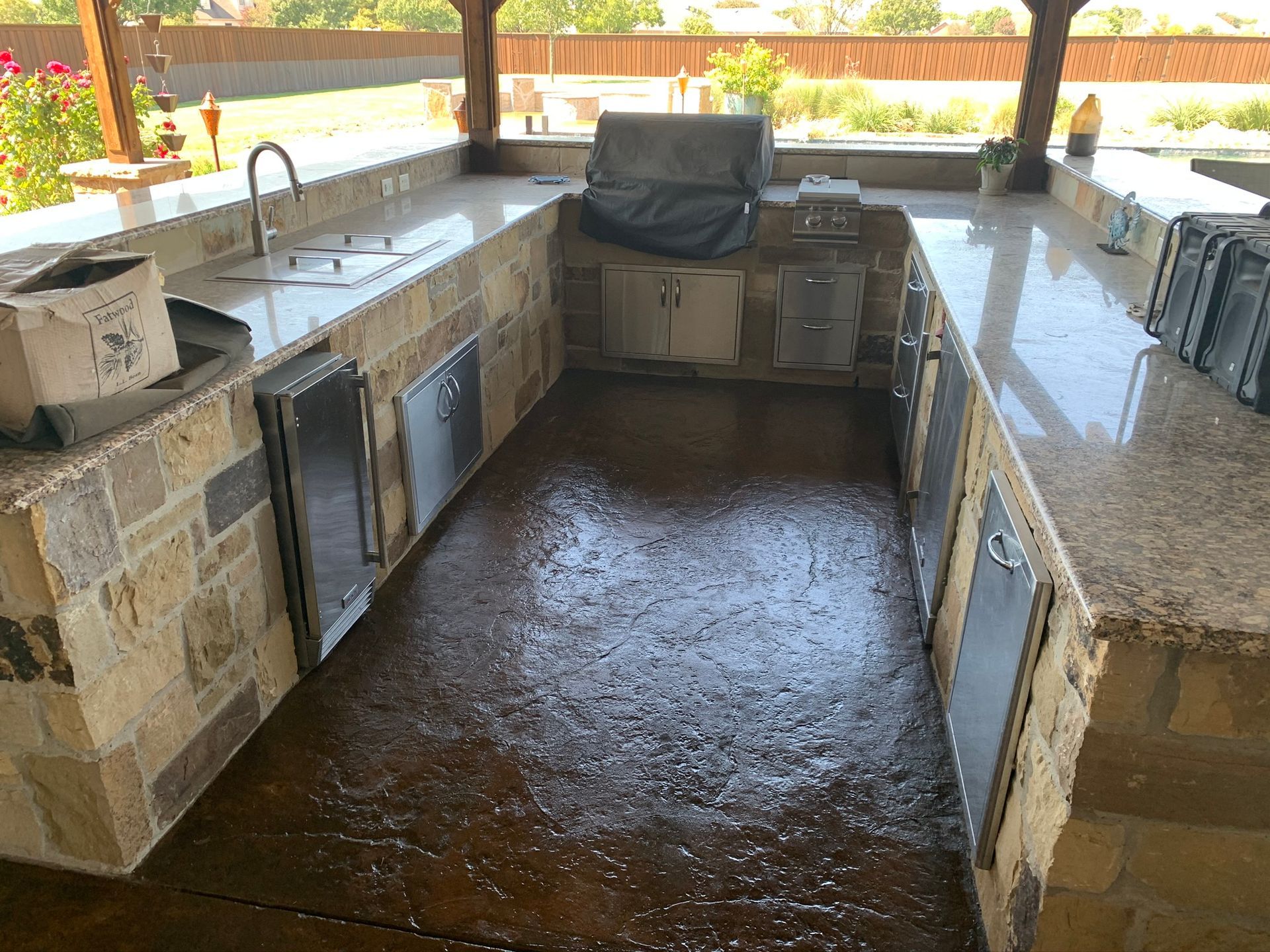 Outdoor kitchen with granite countertops, stainless steel appliances, and stone facing.