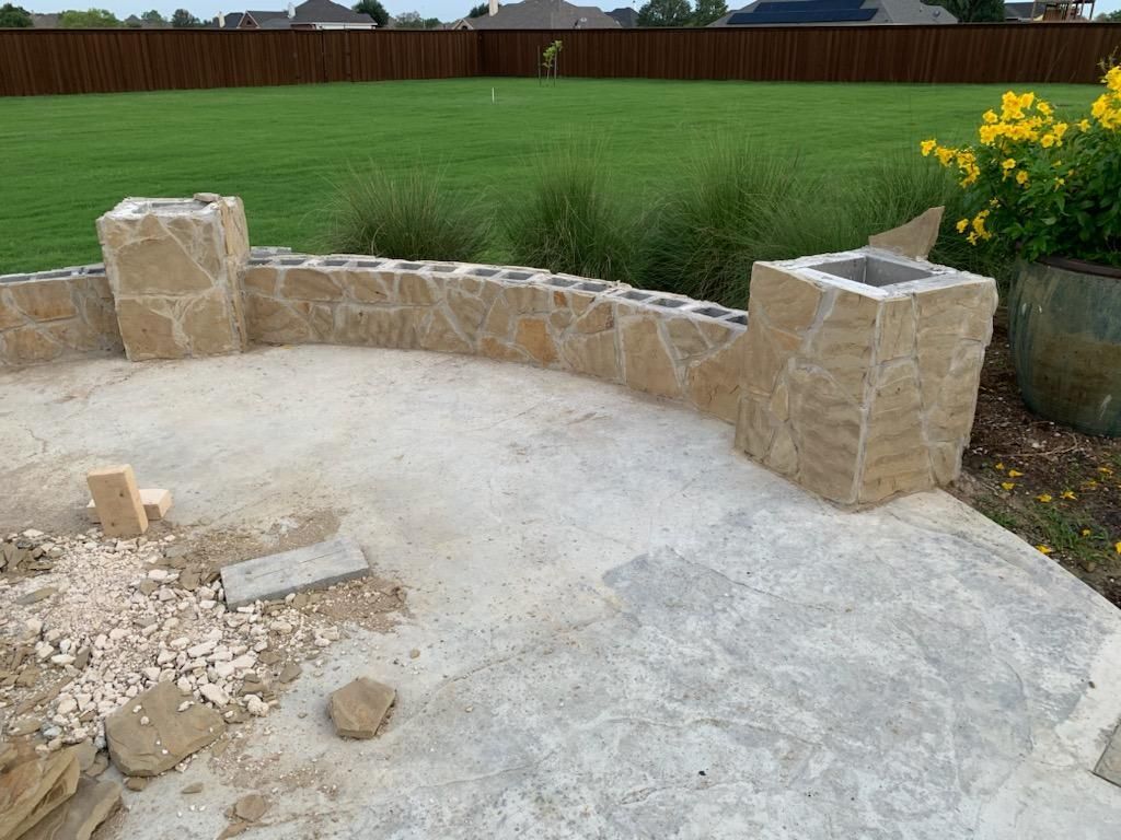Stone patio under construction with retaining wall and grassy background.