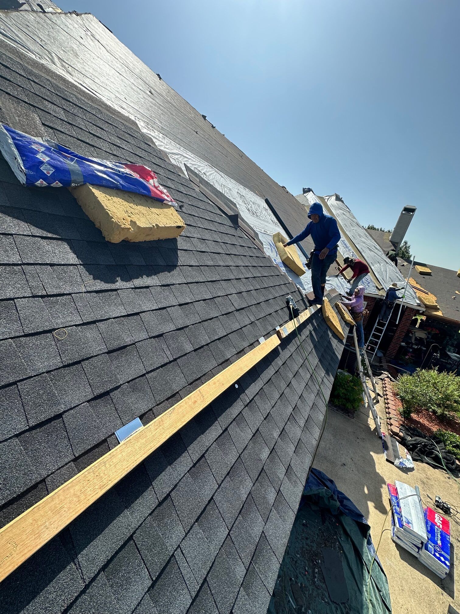 Roofers installing shingles on a house roof under a sunny sky.