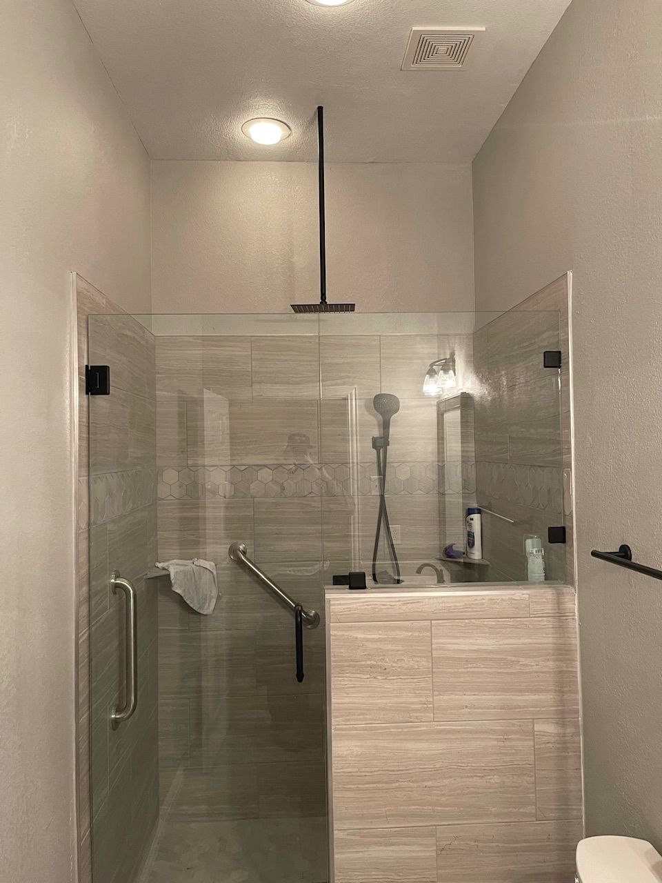 Accessible shower stall with glass doors, grab bar, showerhead, and a small bench.