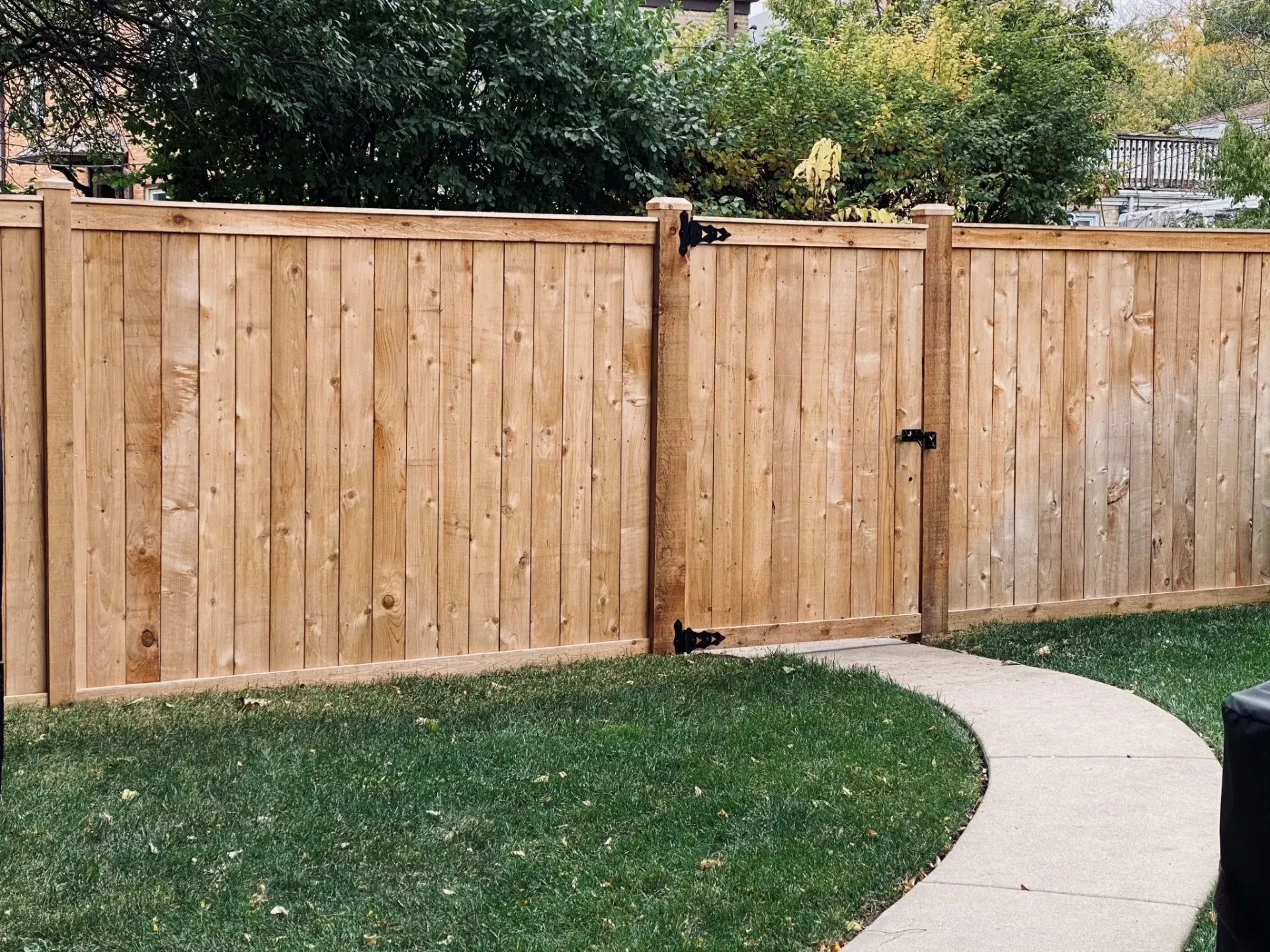 Wooden fence with gate, enclosing a grassy yard. A curved sidewalk leads toward the gate.