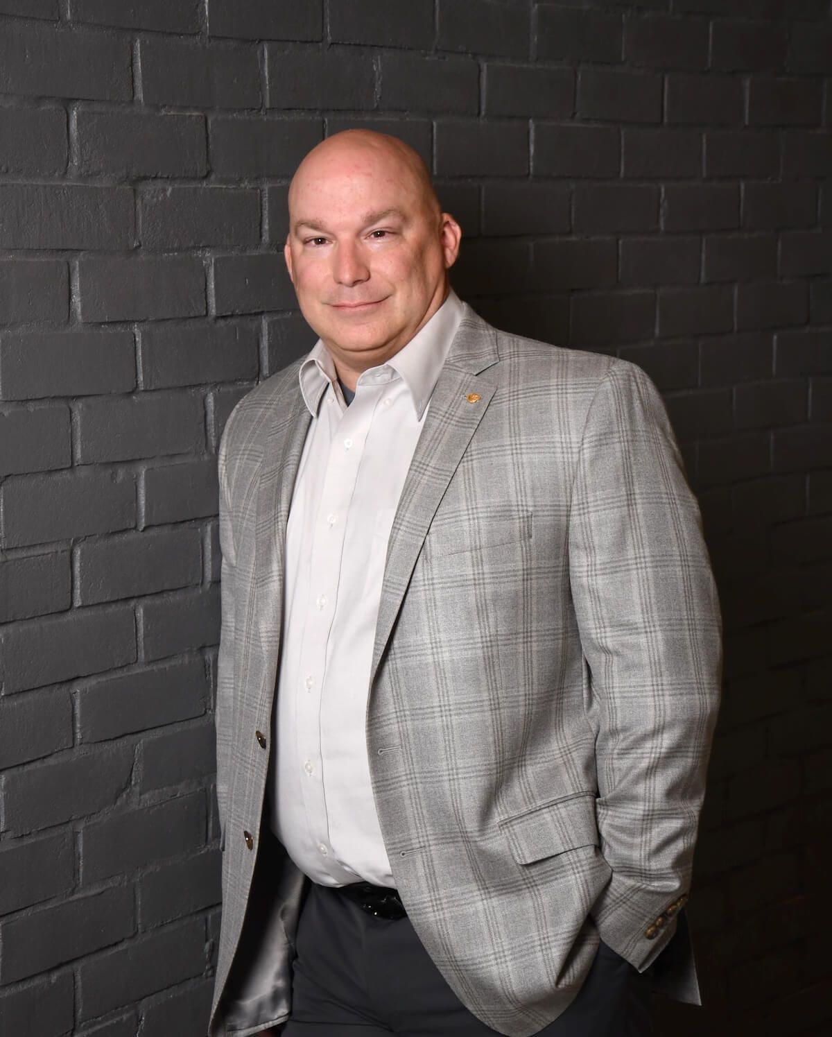 Man in a gray suit standing against a brick wall