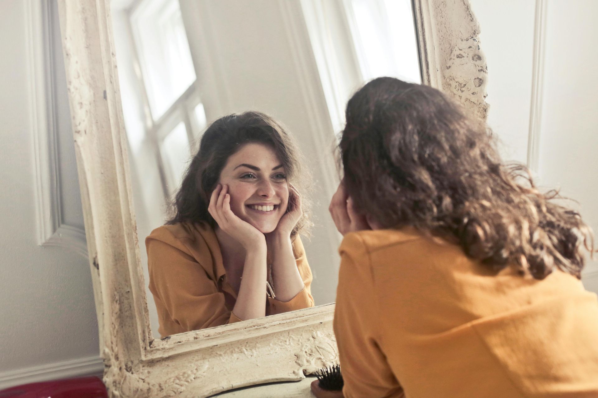 Woman smiling while looking at herself in a large, ornate mirror.