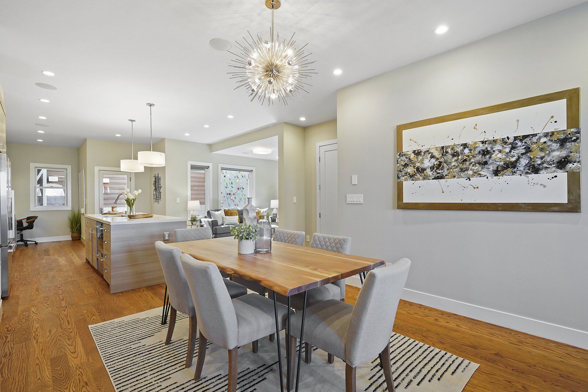 A dining room with a wooden table and chairs and a painting on the wall.