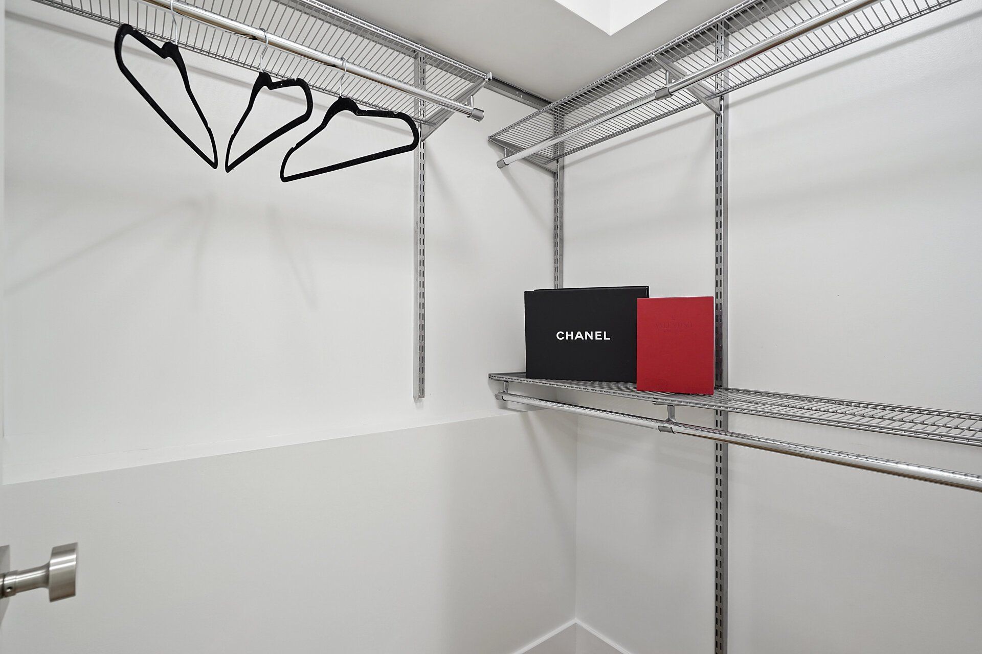 A walk in closet with a chanel box on the shelf.