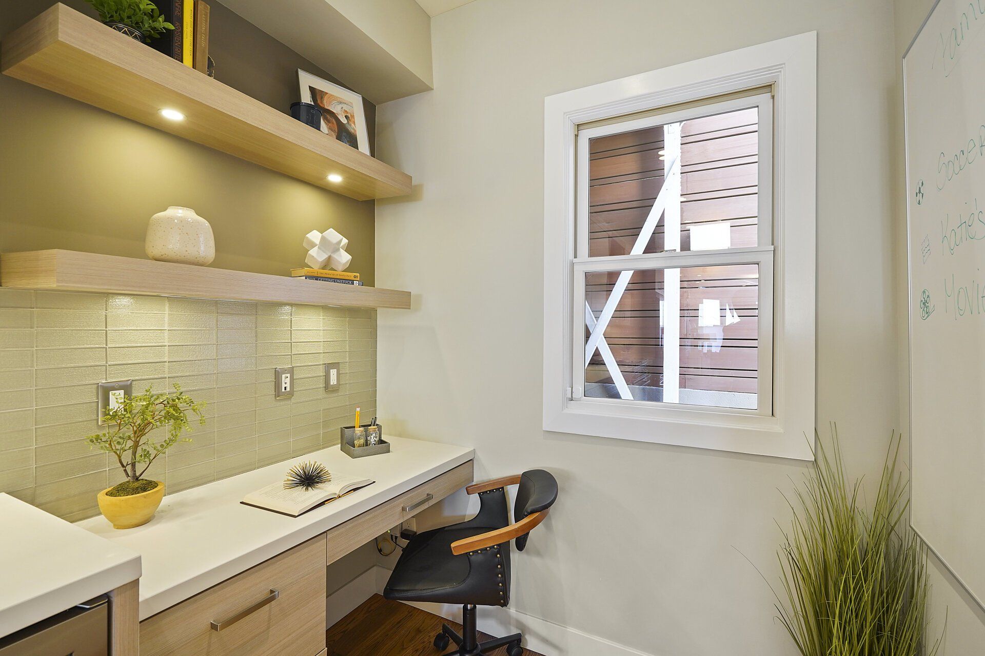 Home office with floating shelves, desk, and a window. A chair sits ready, and a potted plant provides greenery.