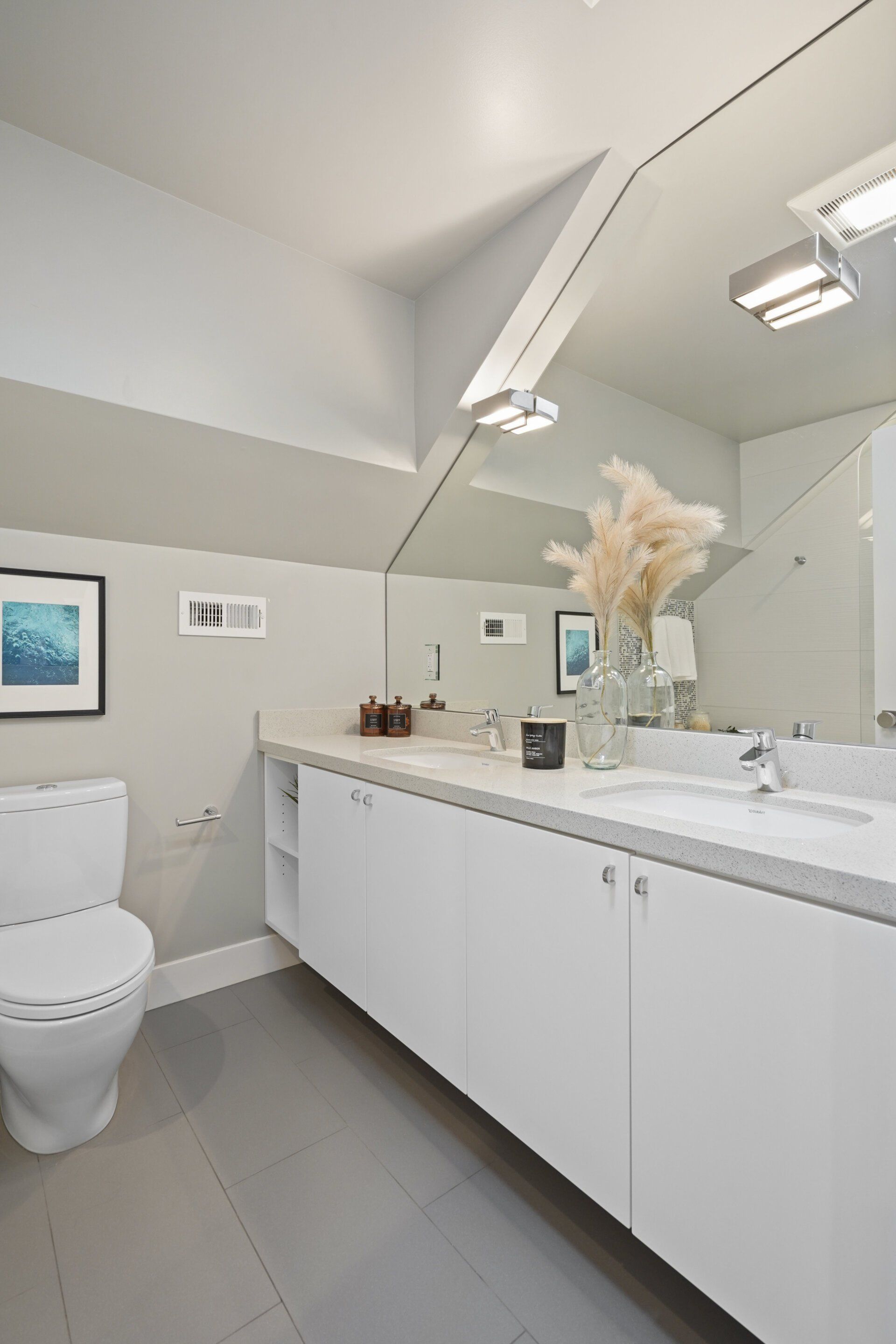 A bathroom with white cabinets and a large mirror. There's a toilet and sink with decorative items on the countertop.