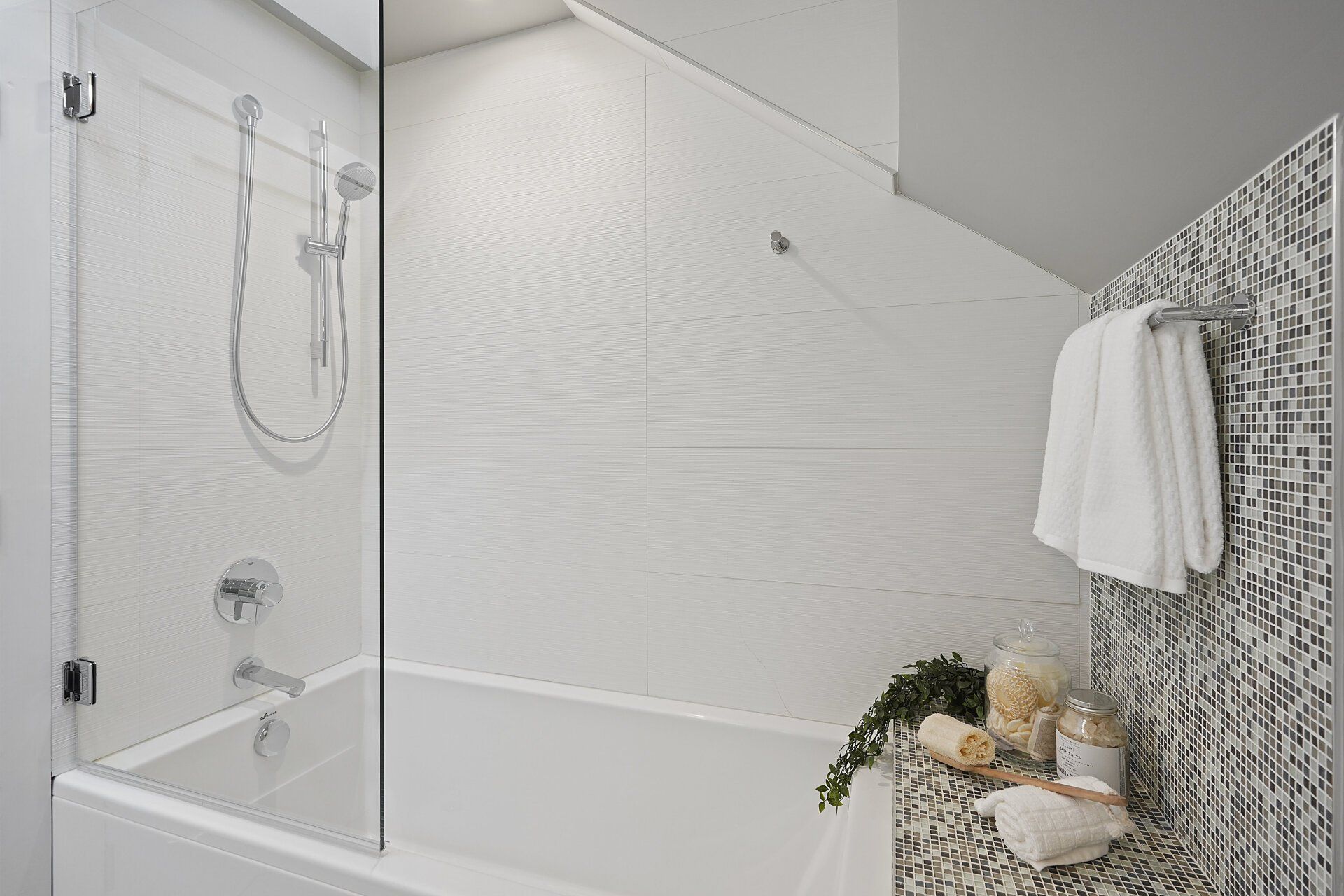 Bright bathroom with glass shower door, tub, and patterned accent wall.  Towels hang from a silver bar.