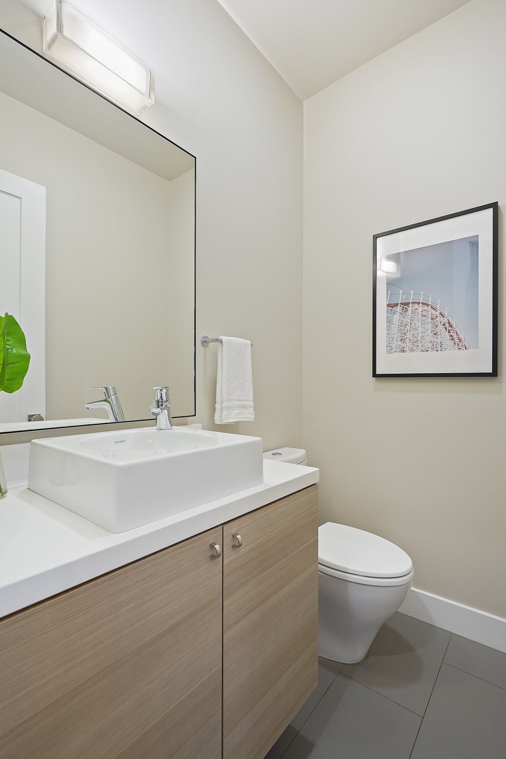 A bathroom with a white sink, light wood cabinet, a toilet, a framed picture, and a large mirror.