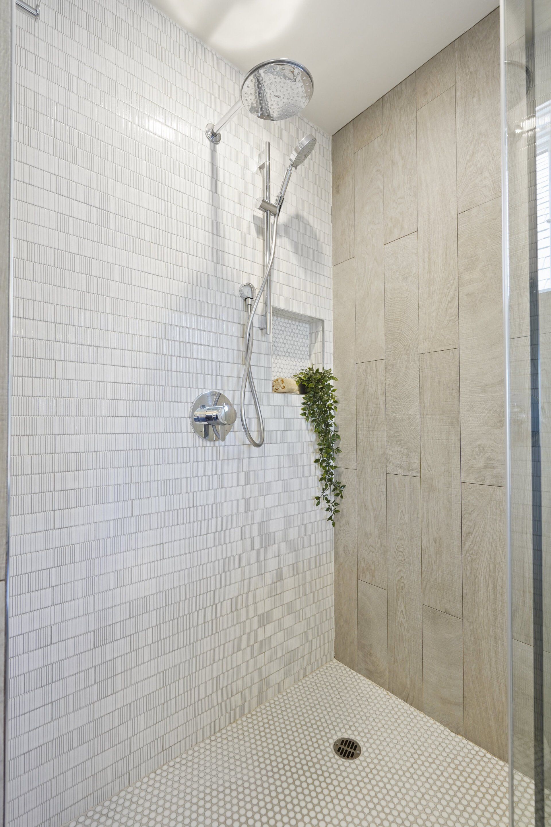 A modern, tiled shower with a rain showerhead and hand shower. White mosaic tile floor and white brick-patterned walls.