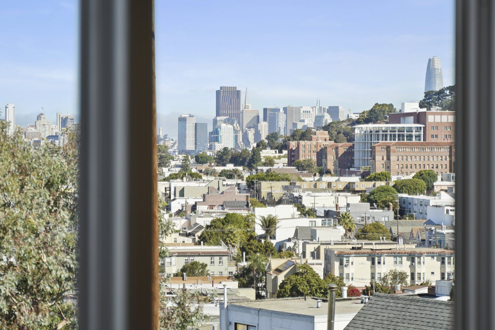 View of San Francisco skyline and residential buildings from a window, with a blue sky.