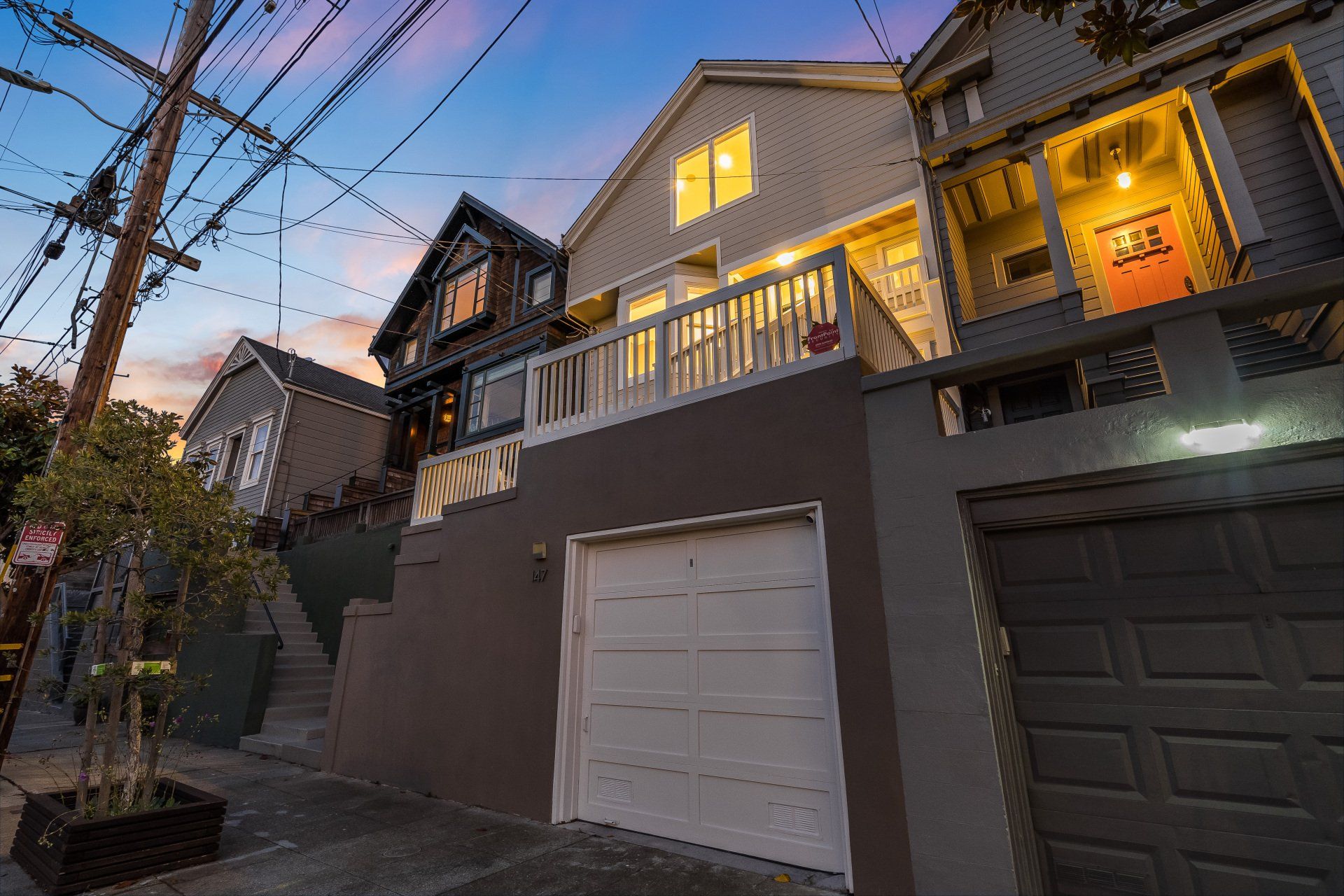 Row of houses at dusk, with a garage and deck. Dark blue and orange sky with lit windows.