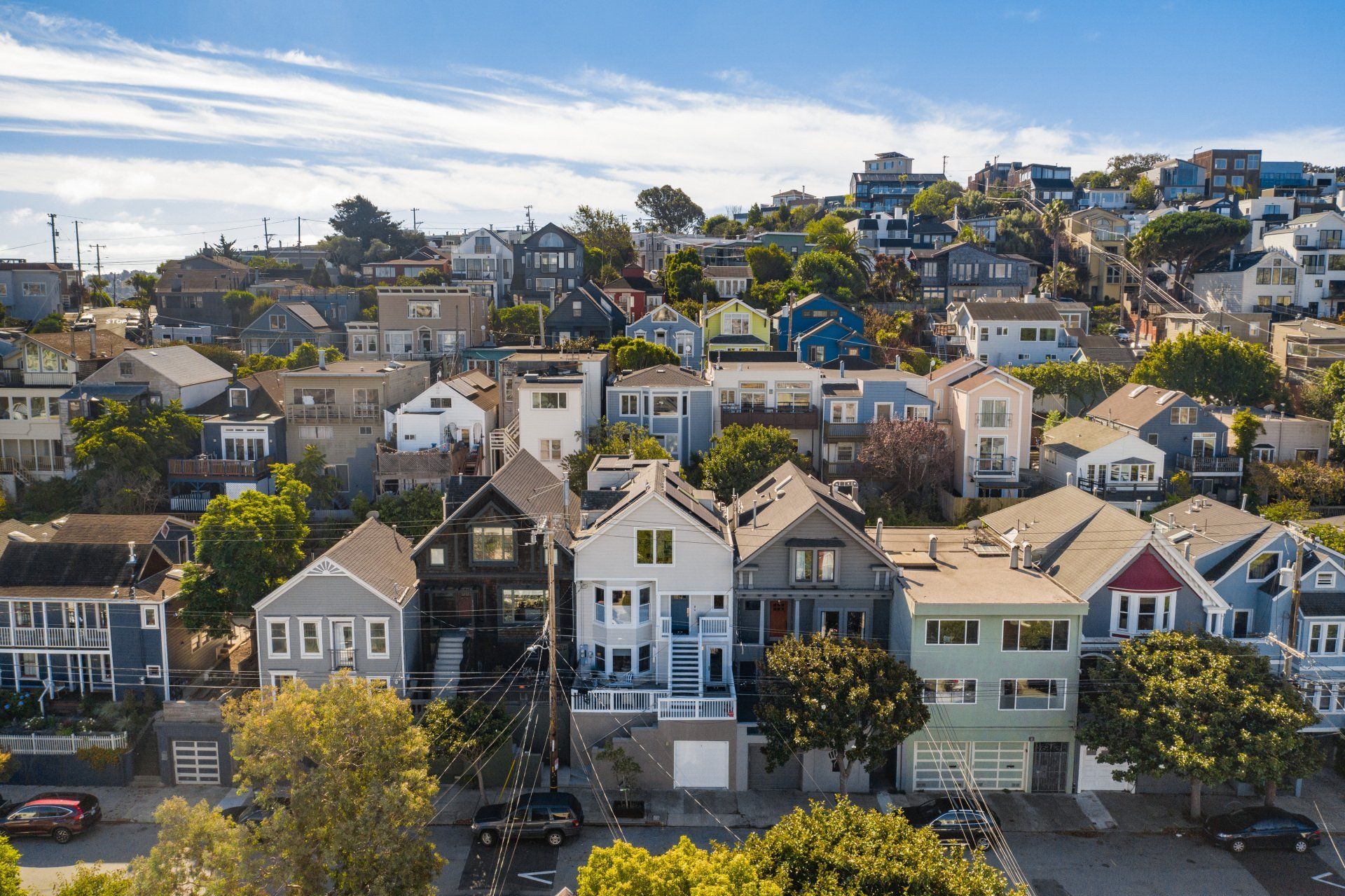 Row of colorful houses on a hillside under a blue sky. Cars parked on street in foreground.