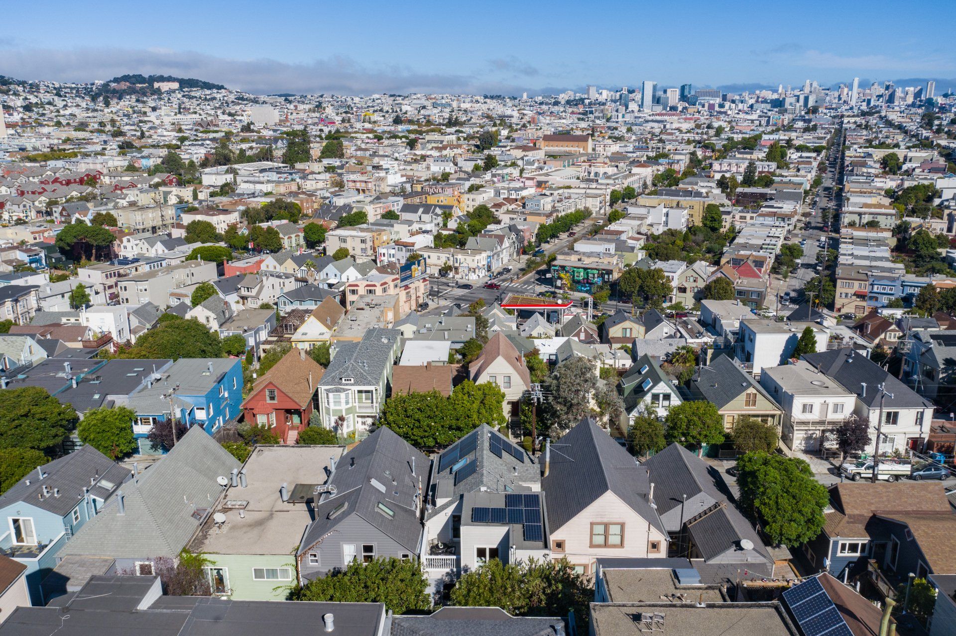 Aerial view of a neighborhood in San Francisco. Houses with various colors and solar panels, stretching toward a distant cityscape.