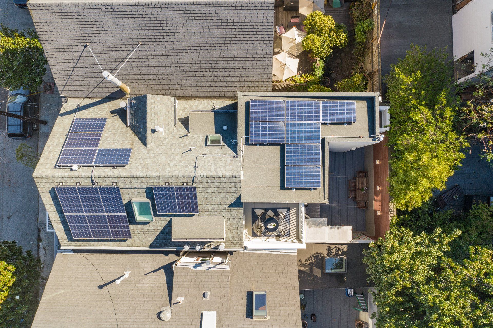 Overhead view of the house with solar panels on the roof, next to a backyard with trees and outdoor seating.