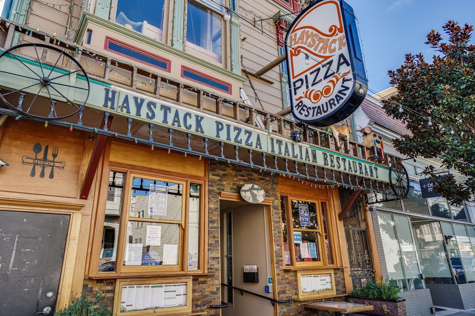 Haystack Pizza Italian Restaurant exterior. Brown and beige facade with a sign and decorative wagon wheels.