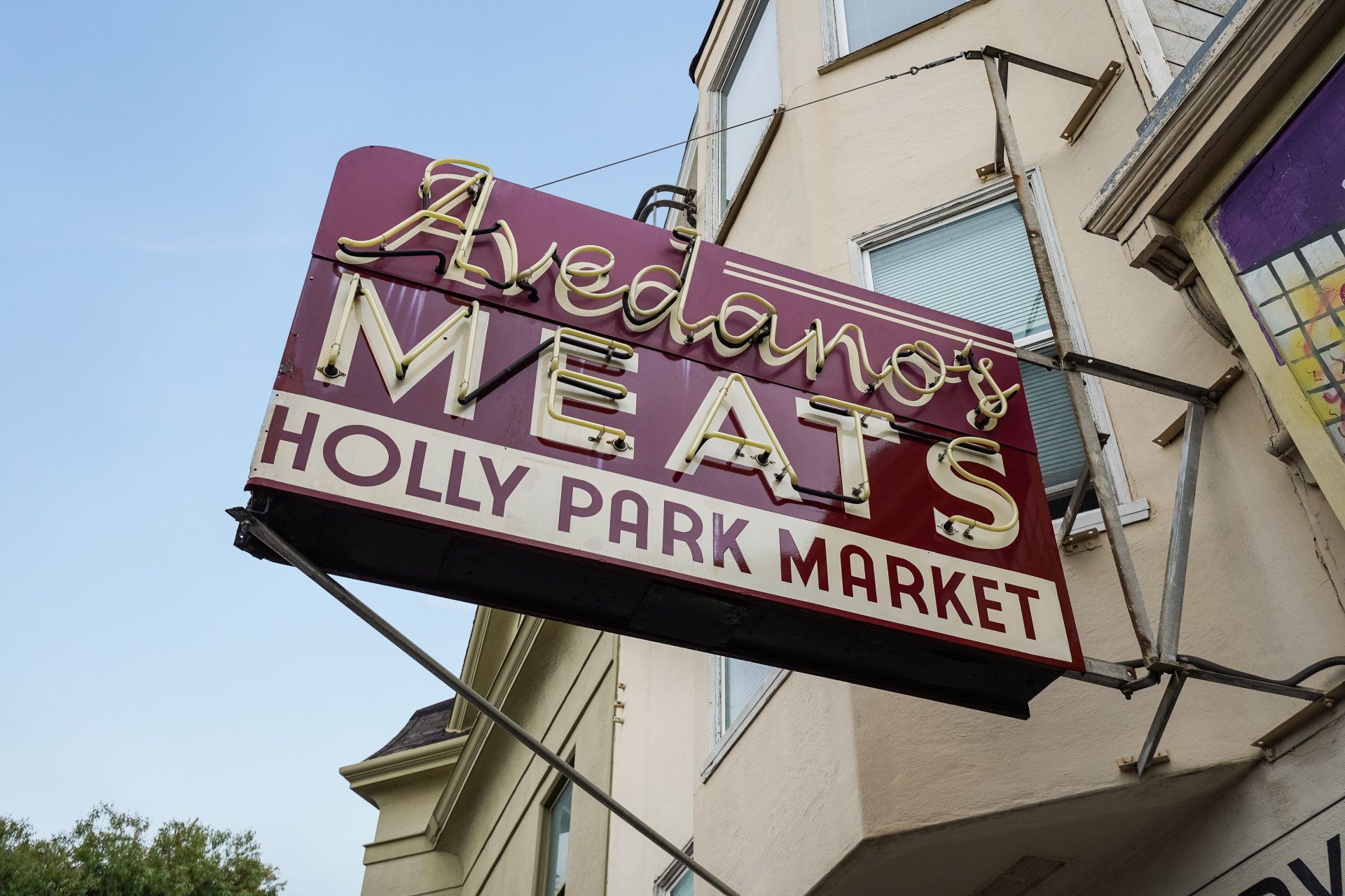Sign for Avedano's Meats at Holly Park Market, a maroon and white neon sign against a building.