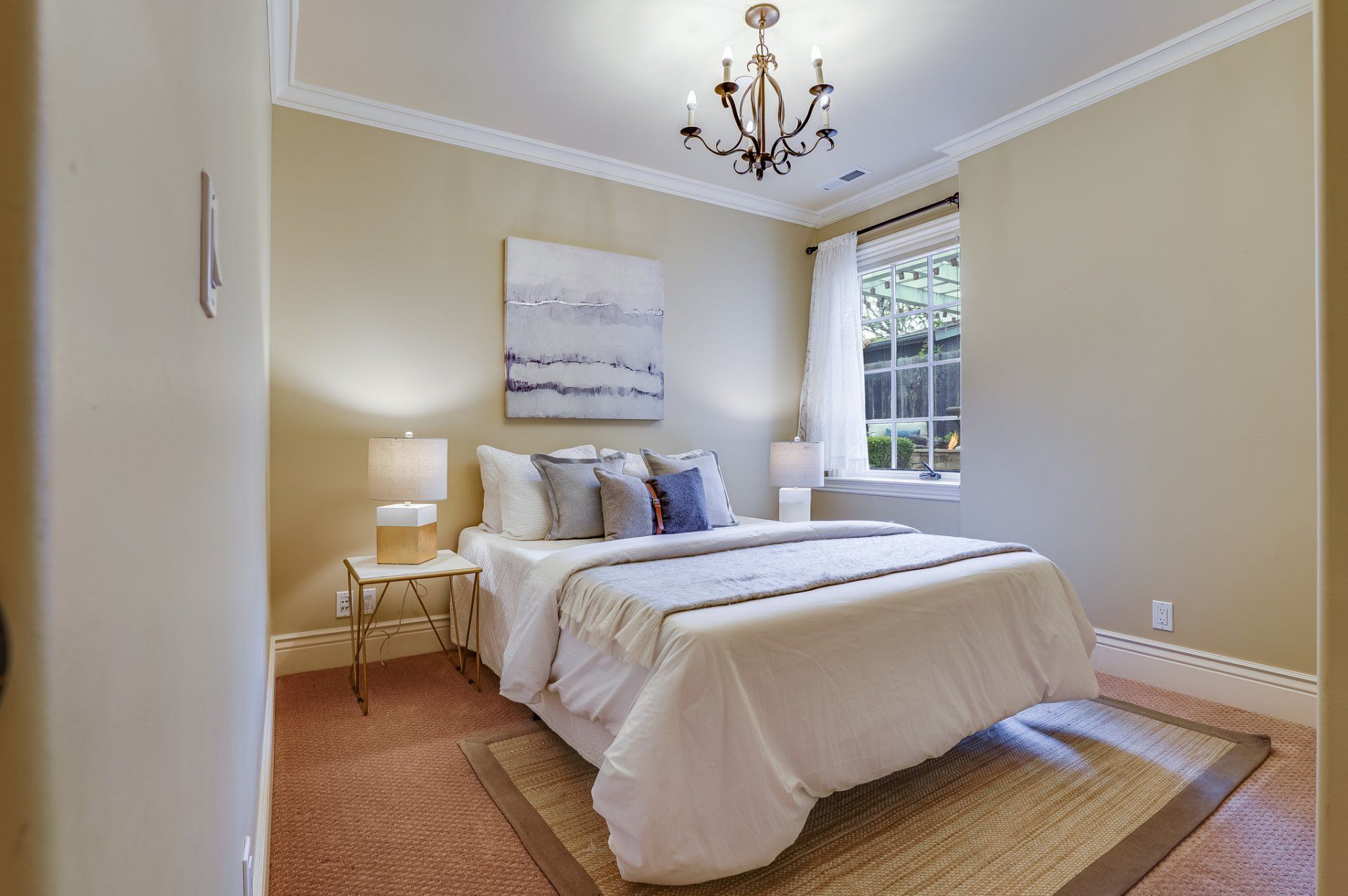 A bedroom with a bed by the window and a chandelier.