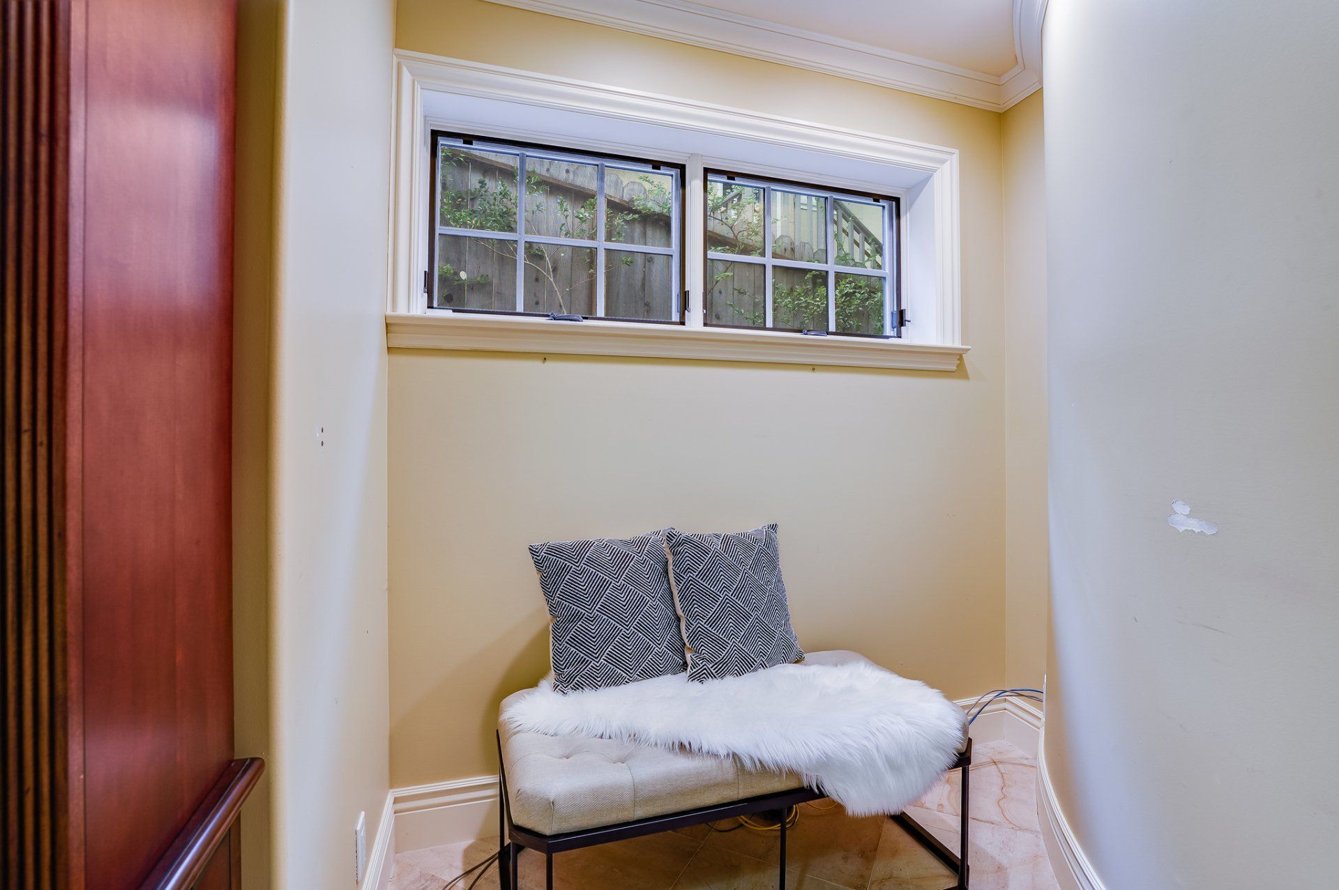 There is a bench in the corner of the room with a window.