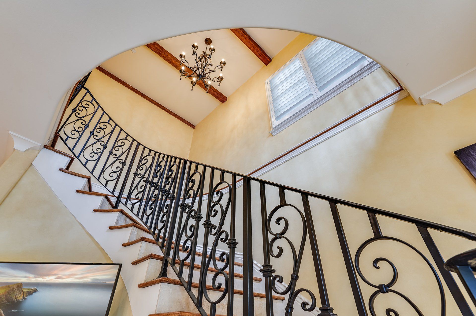 A staircase with a wrought iron railing and a chandelier hanging from the ceiling