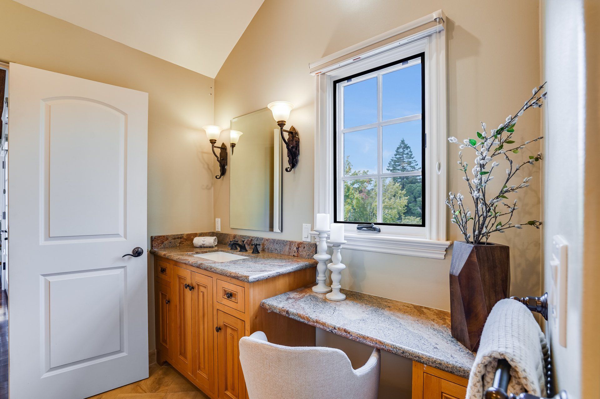 A bathroom with a sink , a desk , a mirror and a window.