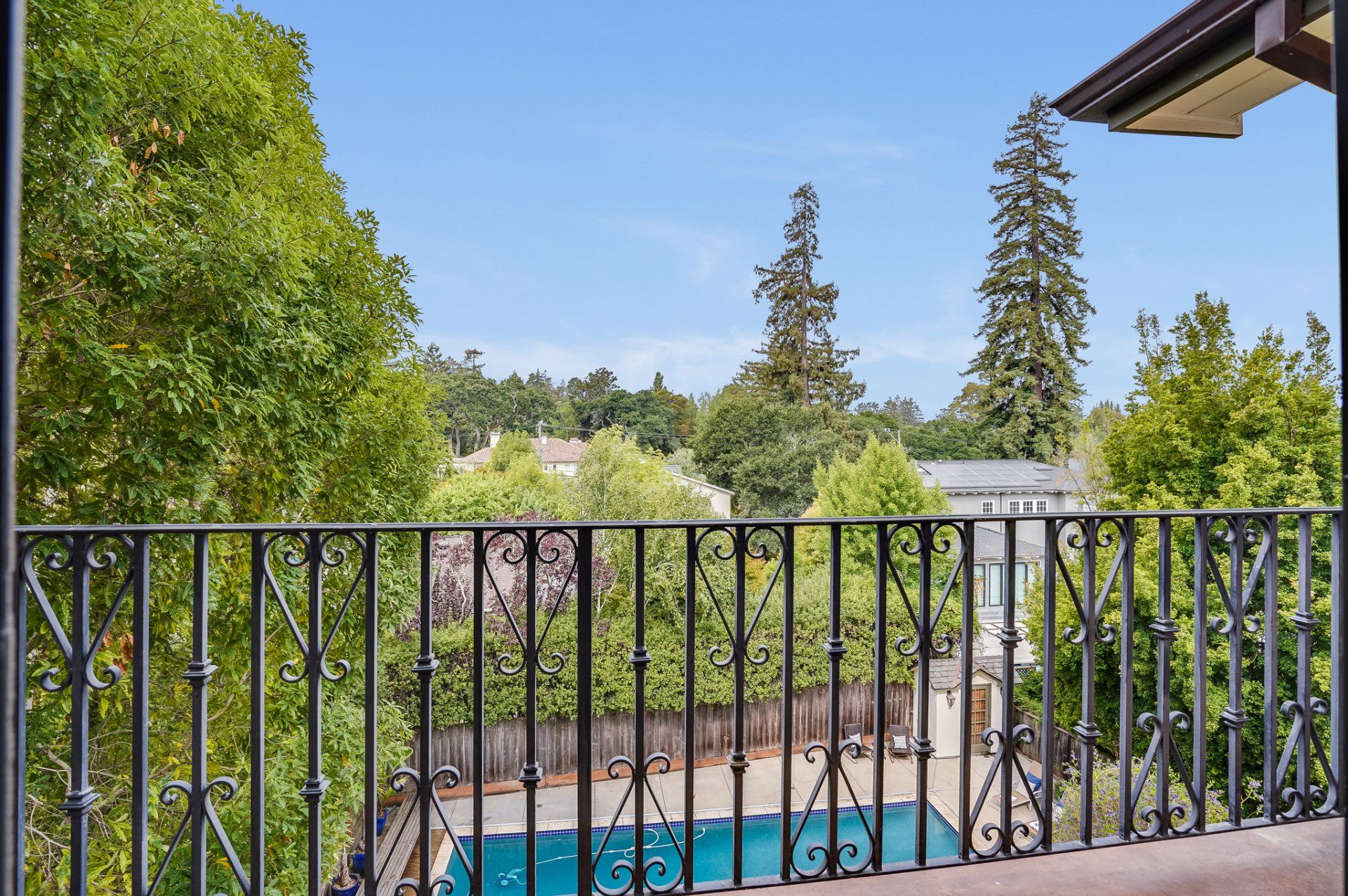 A balcony with a wrought iron railing overlooking a pool and trees.