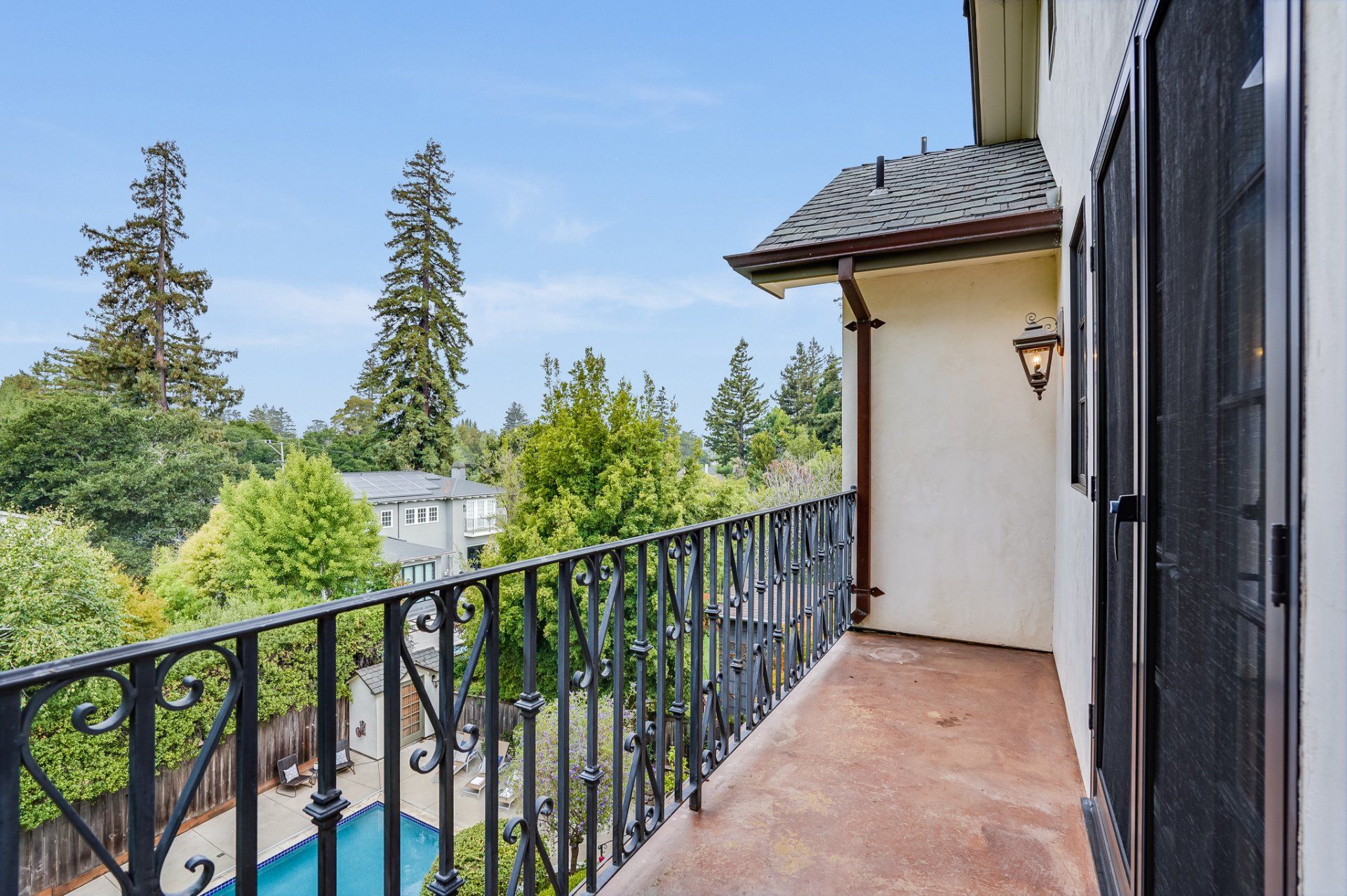 A balcony with a wrought iron railing overlooking a pool and trees.