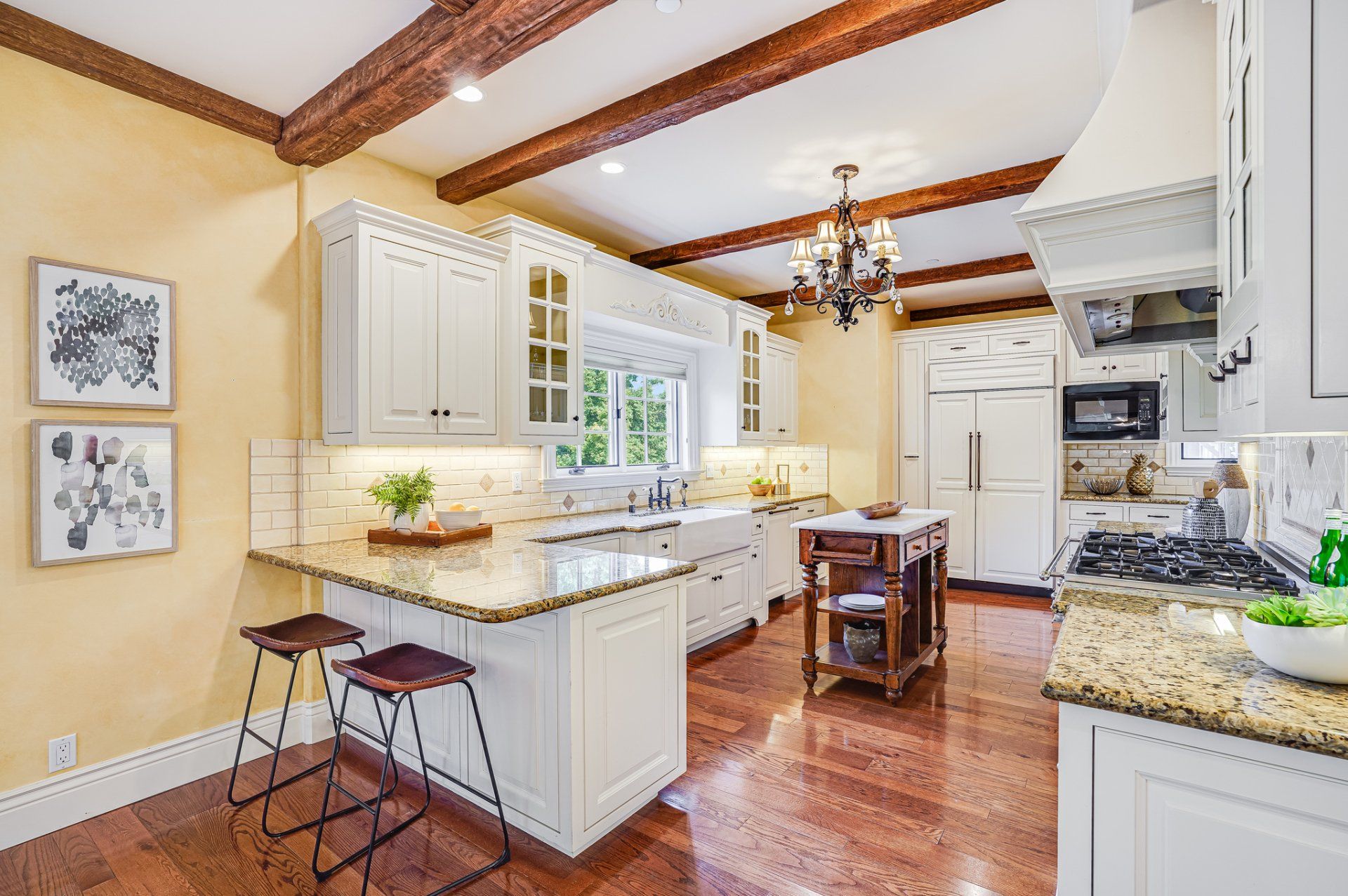 A kitchen with white cabinets , granite counter tops , hardwood floors , and wooden beams.