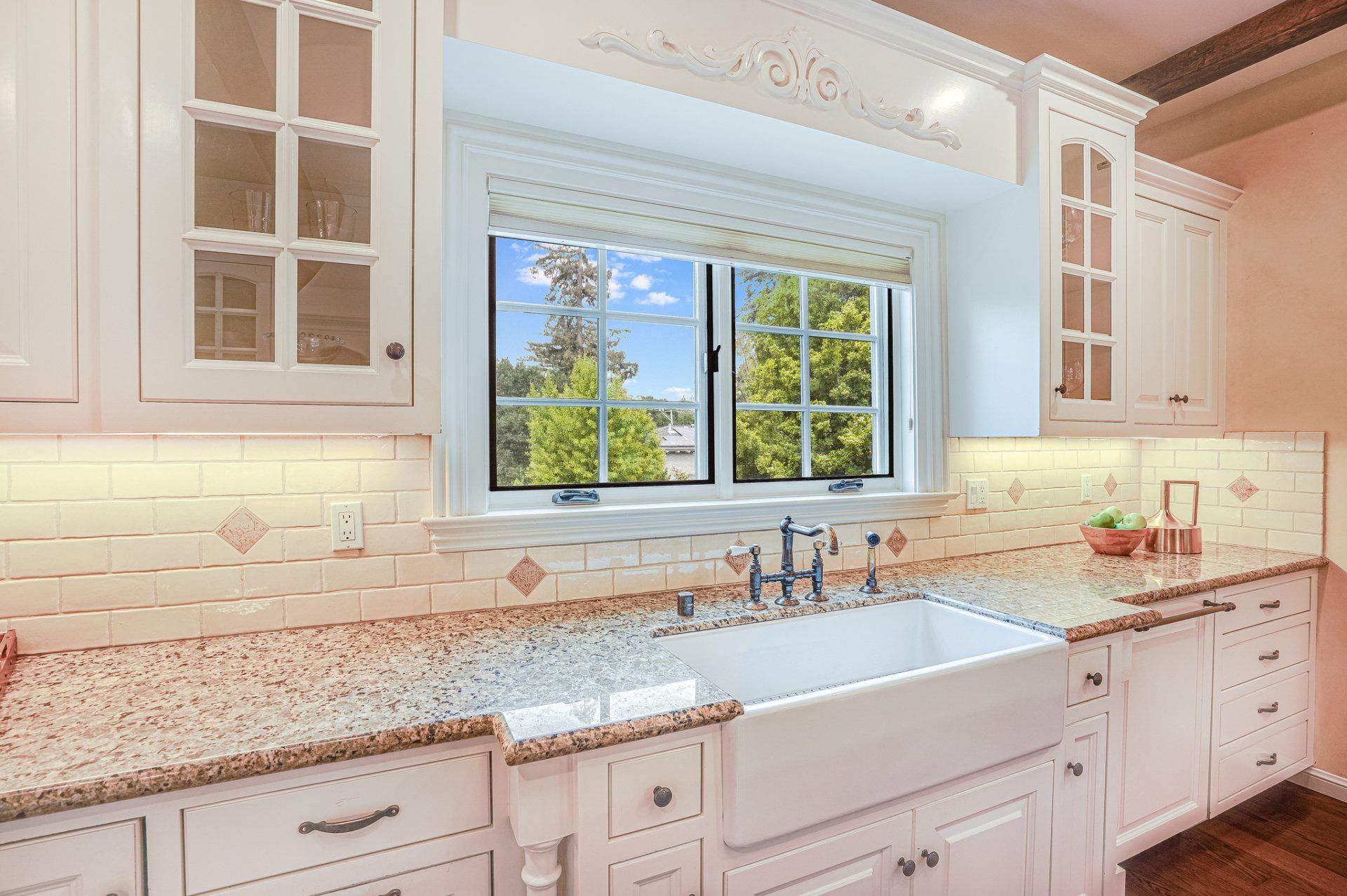 A kitchen with white cabinets , granite counter tops , a sink and a window.
